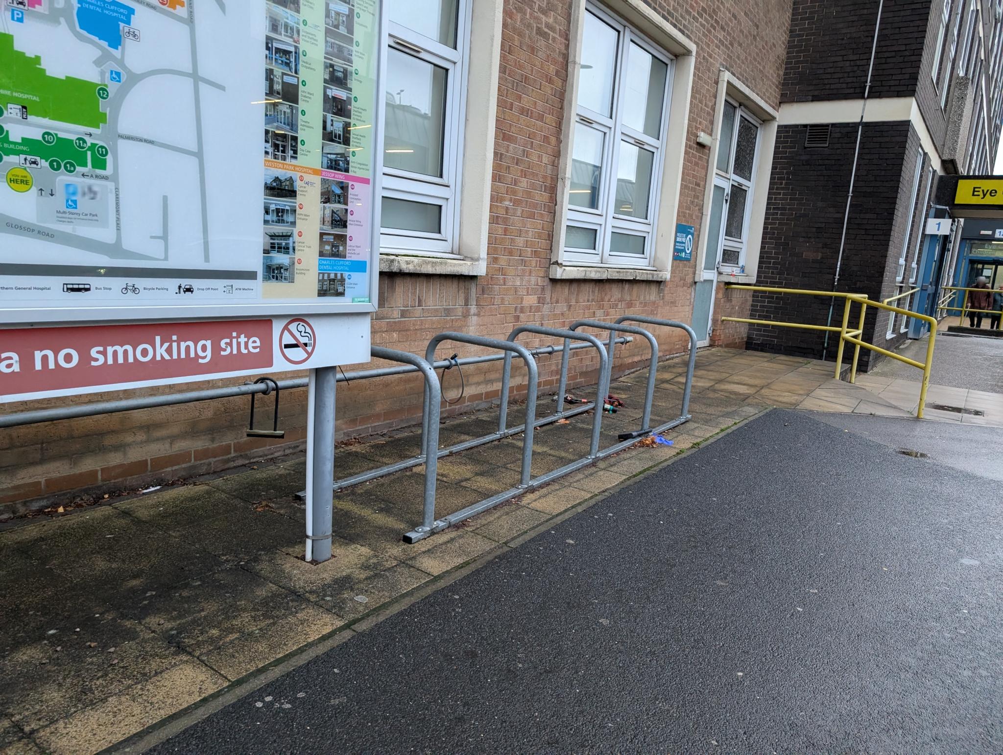 A set of bike stands in front of a building. There is no cover over the stands.